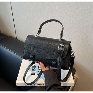 Detail view of black lychee grain leather handbag with silver metal buckles and top handle