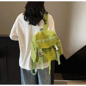 Detail of green nylon backpack showing drawstring closure and silver metal buckles on back