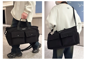 Detail of black travel bag showing dual front buckle pockets and adjustable shoulder strap