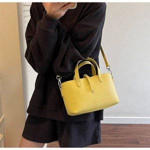 Model wearing a yellow lychee-textured crossbody bucket bag with silver metal buckles