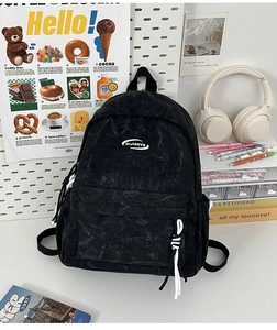 Close-up of black corduroy backpack with front pocket and woven zipper puller detail