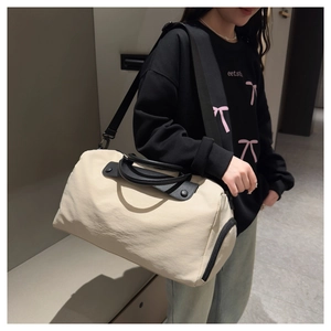 Detail view of large cream travel bag with black leather handles and adjustable strap