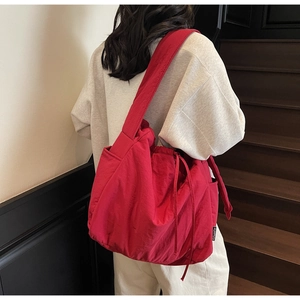 Detail of red large capacity nylon tote bag with drawstring closure on model shoulder