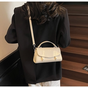 Detail of minimalist cream crossbody bag with leather texture and detachable strap on model