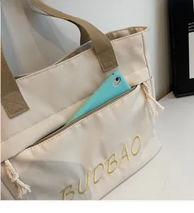 Detail of the front zipper pocket on a beige canvas tote bag holding a green mobile phone