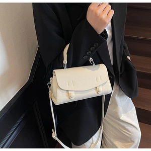 Chic beige lychee grain leather crossbody bag styled on dark wooden stairs