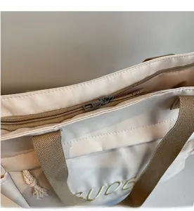 Close-up of smooth metal zipper and embroidered detail on beige canvas tote bag