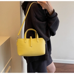 Detail of yellow lychee texture leather handbag featuring crossbody strap and metal buckle
