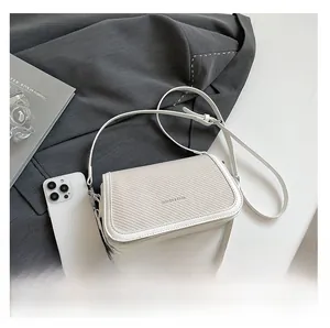 Detail of white crossbody bag with beige woven texture next to a grey suit and accessories
