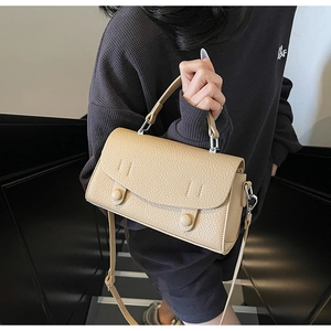 Dettaglio della borsa in pelle beige con texture litchi e fibbie rotonde su modella