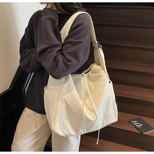 Detailed shot of large cream canvas shoulder bag featuring adjustable strap and drawstring closure