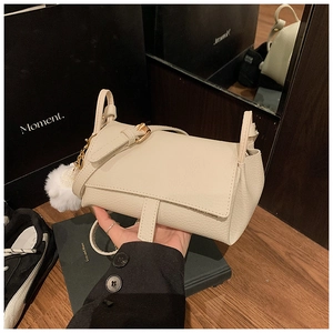 Close-up of cream pebble grain leather crossbody bag with gold buckle and fuzzy pom-pom