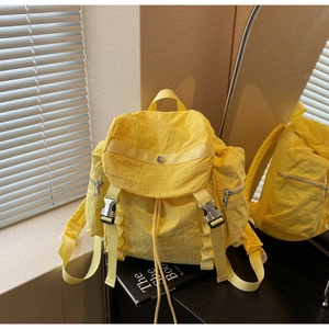 Detail view of yellow nylon backpack featuring silver metal buckle and side zipper pockets