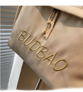 Detail of BUDBAO embroidered lettering and fringe tassel zipper on beige canvas shoulder bag