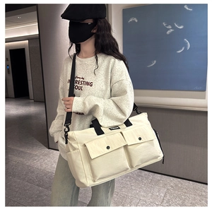 Travel tote bag featuring dual front flap pockets and adjustable black shoulder strap