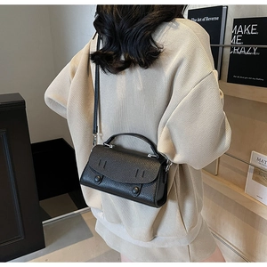 Detailed view of black litchi texture leather crossbody bag on a beige sweater