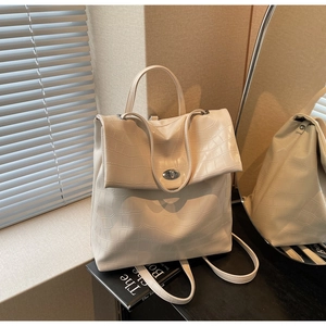 Detalle de mochila crema con grabado de cocodrilo, cierre giratorio de metal y asa