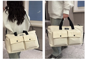 Detail view of large cream travel bag featuring double front pockets and adjustable shoulder strap