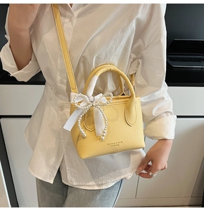 Detail of yellow bucket bag with lychee texture, silk bow, and pearl charms