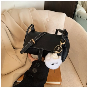 Detail of black crossbody bag with white contrast stitching and cute plush monster charm