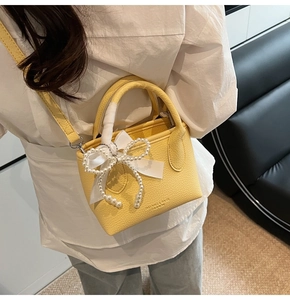 Detail of yellow mini tote bag featuring lychee texture and pearl bow charm accessory