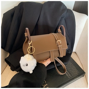 Detail of brown litchi leather bag with magnetic flap and white pompom charm