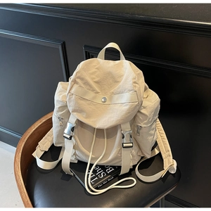 Detail of cream nylon backpack featuring multiple pockets and silver metal buckles