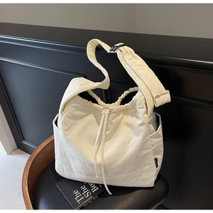 Detail of a beige canvas shoulder bag with drawstring closure and side pockets