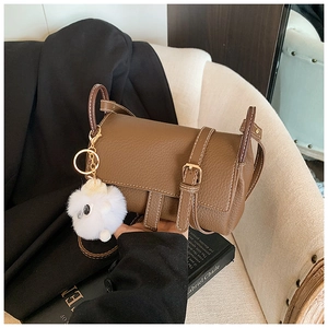 Detailed view of a brown pebbled leather crossbody bag with white stitching and fuzzy pompom charm
