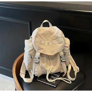 Detail of off-white nylon backpack with metal buckles and drawstring on black chair