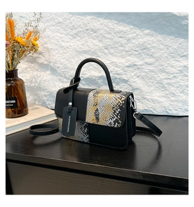 Détail d'un sac bandoulière élégant en peau de serpent noir et doré avec étiquette mode