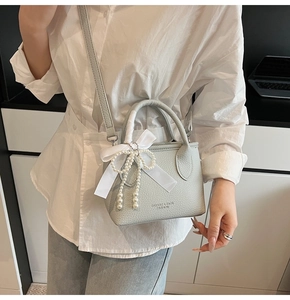 Detail of light blue lychee leather handbag with silk bow and pearl charm on a model