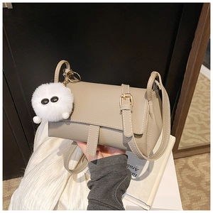 Close-up of khaki pebbled leather shoulder bag with a cute plush monster charm