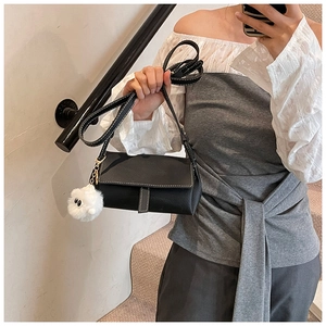 Detail of black crossbody bag with white stitching and a white pompom charm