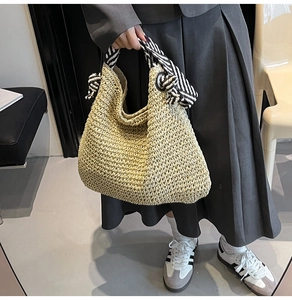 Détail d'un sac cabas en paille tressée avec foulard décoratif rayé noir et blanc sur l'anse