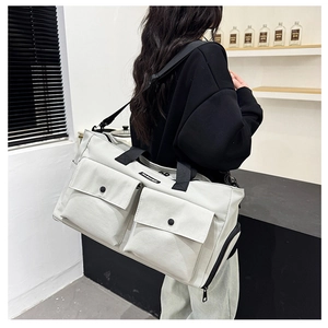 Rear view of the large white canvas travel bag with black straps worn by a model