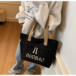 Detail of black canvas tote bag showing BUDBAO embroidery and khaki carrying straps