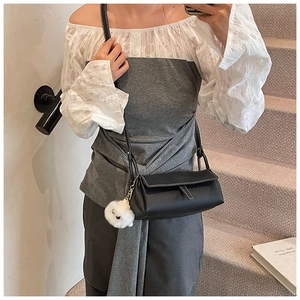 Close-up of black pebbled leather crossbody bag with white stitching and plush charm