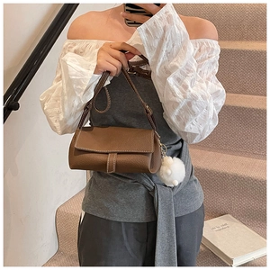 Close-up of brown litchi grain leather handbag with contrast stitching and plush charm