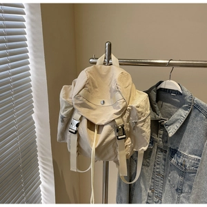 Detail view of cream nylon backpack with multiple pockets and drawstring on metal rack