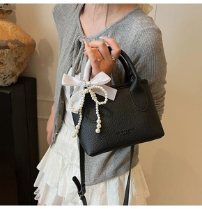 Detail view of black lychee grain bucket bag with pearl tassel and satin bow charm