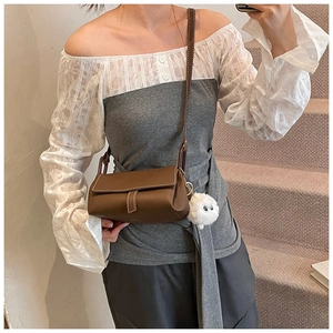 Detail of brown leather crossbody bag with contrast stitching and plush keychain