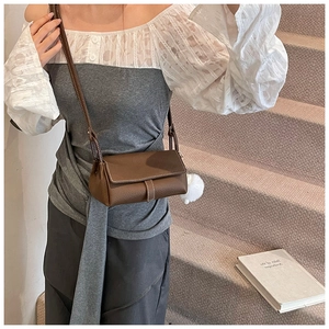 Detail view of brown textured leather crossbody bag with white plush ball charm accessory