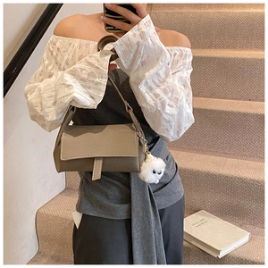 Detail of grey leather shoulder bag with decorative strap and white plush ball charm