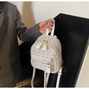 Détail d'un mini sac à dos en tweed blanc avec zips dorés et texture tissée en main