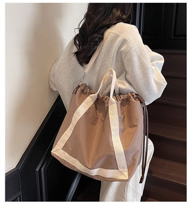 Detail of a khaki drawstring tote bag featuring cream webbing straps and silky nylon texture