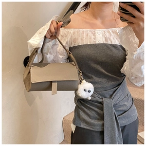Close-up of grey pebbled leather handbag with white stitching and plush toy charm