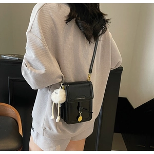 Close-up of black leather crossbody bag featuring gold hardware and a plush bear charm