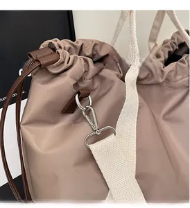 Detail view of khaki nylon tote bag featuring high-shine silver hardware and cream strap