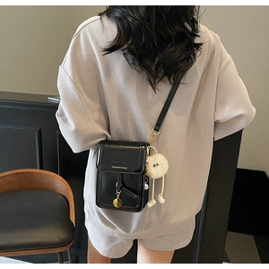 Detail of black leather crossbody phone bag with FASHION & BAGS text and plush pompom